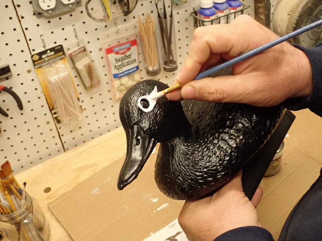Painting the eye of a duck decoy on a work bench.