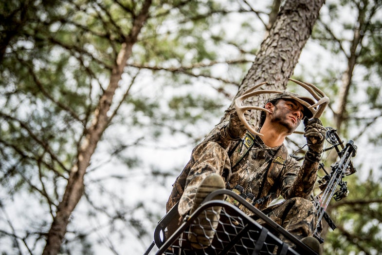 Deer hunter in a treestand rattling antlers.