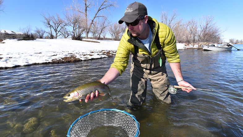 angler holds trout in front of snowy riverbank