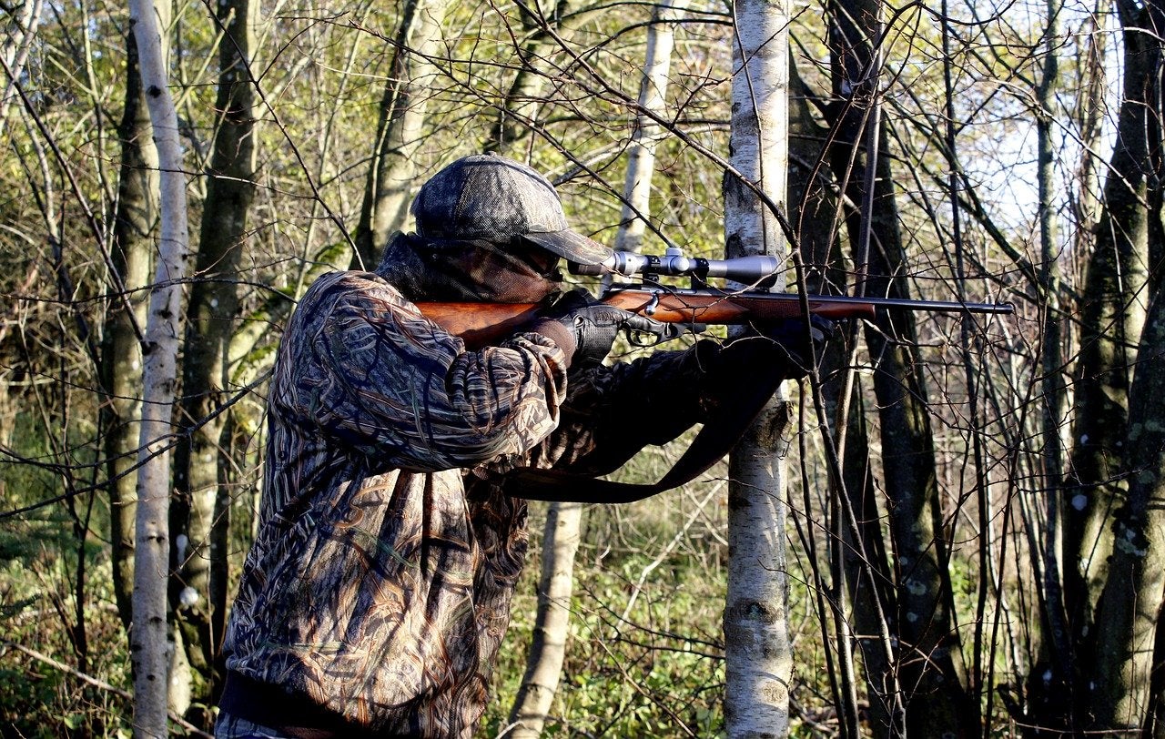 Hunter shooting a rifle while leaning against a tree.