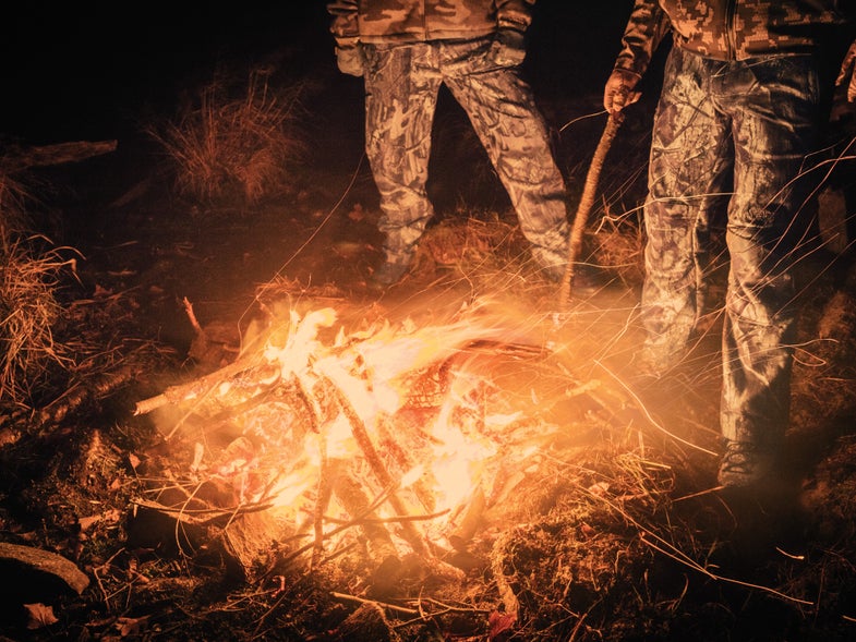 Two Hunters tend the perfect campfire at night.