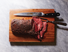 A venison backstrap cooked sous vide resting on a cutting board with a knife and carving fork.
