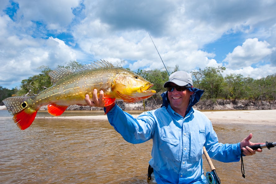 Charlie Conn caught this 15-pound peacock bass while hosting a flyfishing excursion in Roraima, Brazil. The colorful and powerful fish were hitting large streamers and poppers fished on 8- and 9-weight rods. "The smile says it all," says Conn. "When you fish for a month straight, the surroundings and relationships define the trip as much as the fishing." The anglers stayed in a floating lodge that moved along tributaries of the Amazon basin each day. "It reminded me of when I was a kid fishing for largemouths," says Conn's fishing buddy, photographer Brian Grossenbacher. "The only difference is these bass were 10 to 15 pounds heavier. It was truly one of the most amazing experiences of my life."<br />
<strong>Location:</strong> River X, Brazil<br />
<strong>Issue:</strong> July, 2010<br />
<em>Photo by Brian Grossenbacher</em>