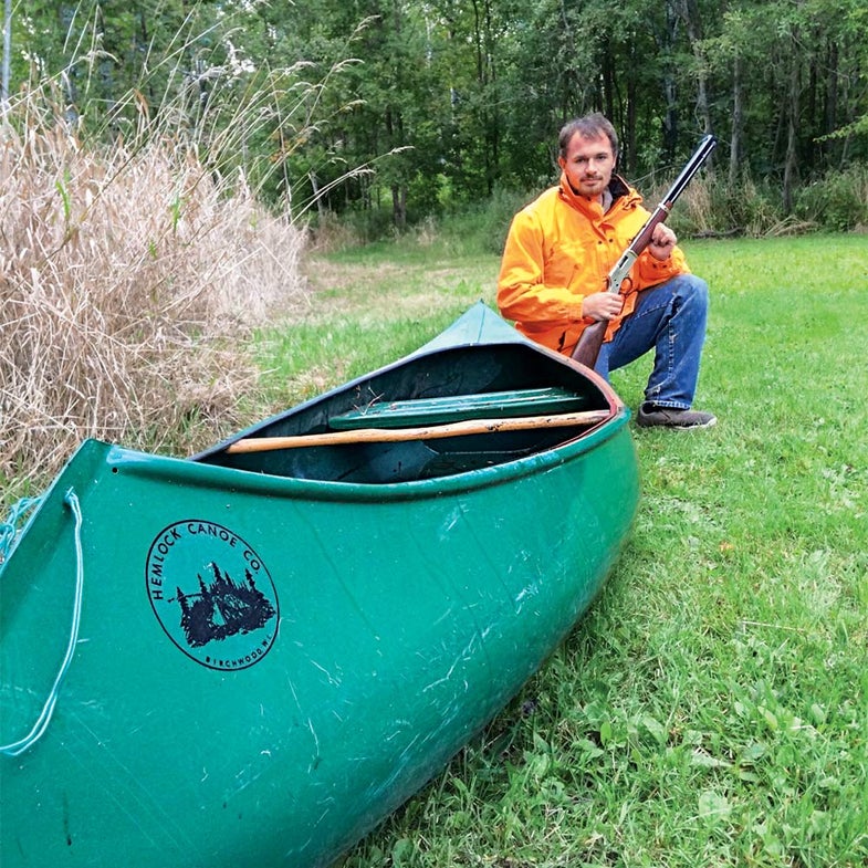Hunter with a gun kneeling by canoe