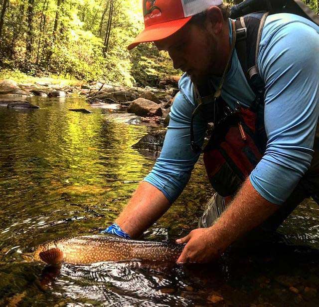 fisherman holding a trout in a stream