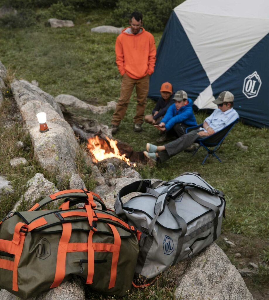 camping gear bags on a rock near men at campfire