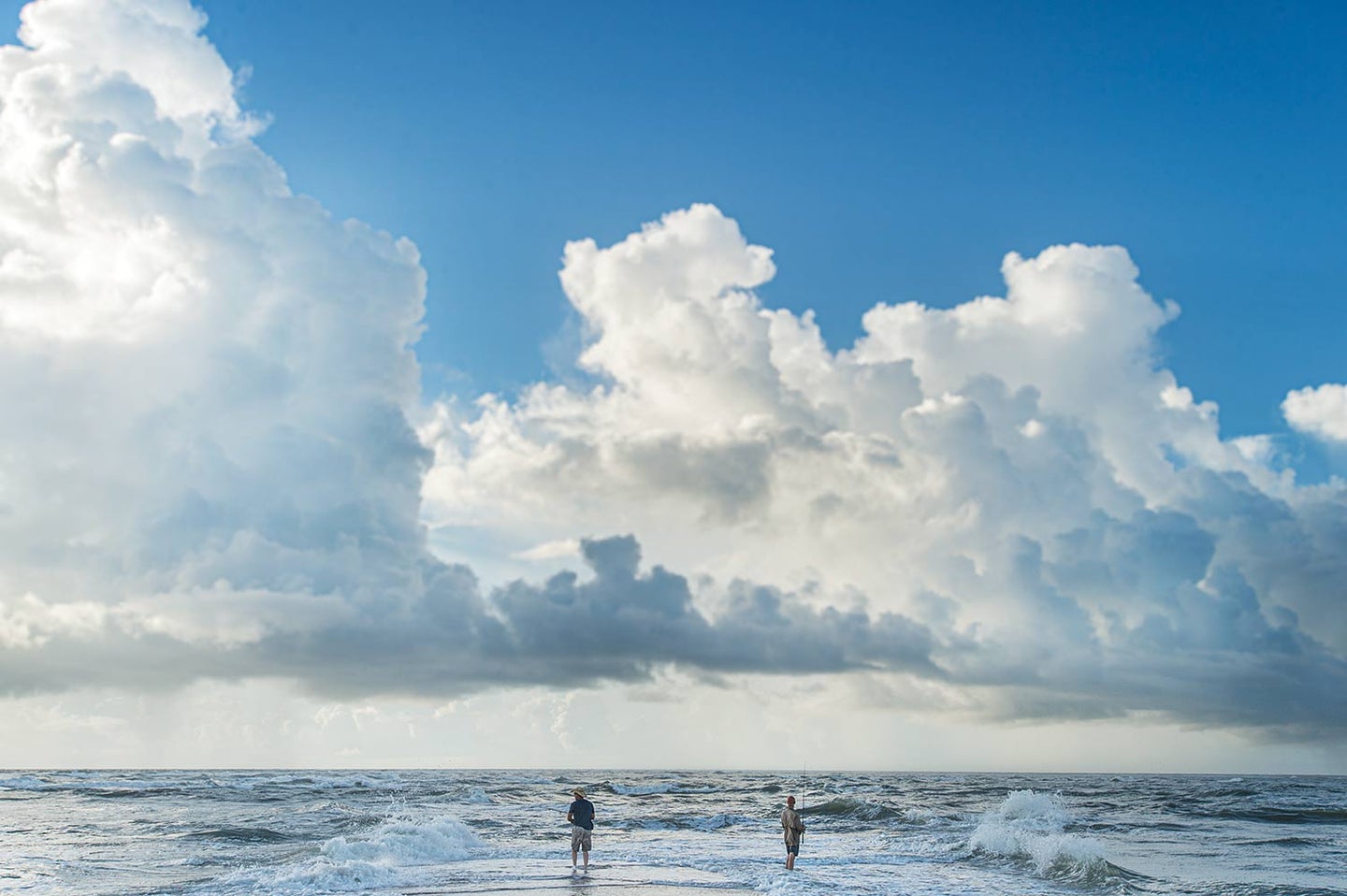 Two people standing in the surf while fishing.
