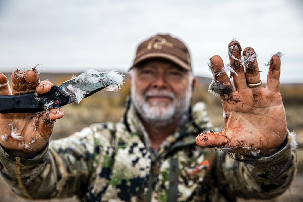 A hunter with duck feathers on his hands.