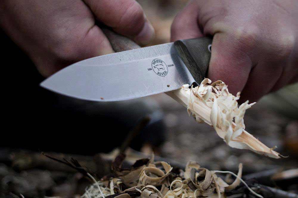 The White River Ursus 45 buchcraft knife scraping a branch of wood.