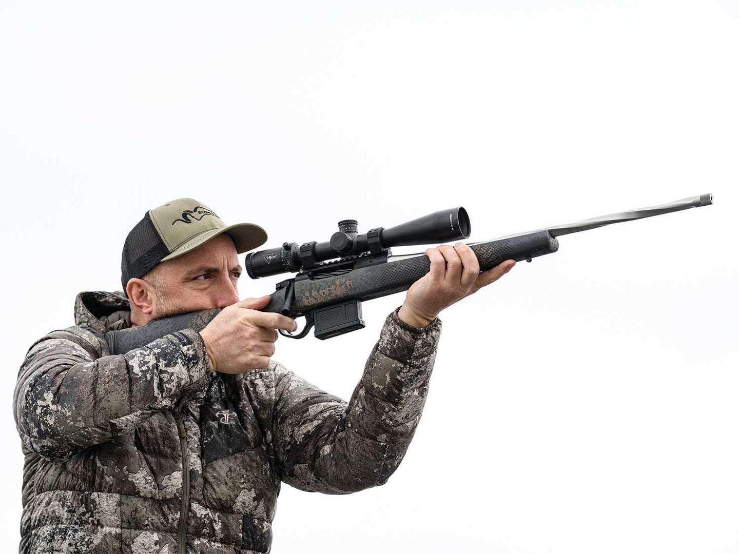 An author aiming a custom Lapua rifle with a scope.