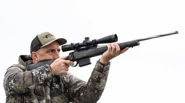 An author aiming a custom Lapua rifle with a scope.