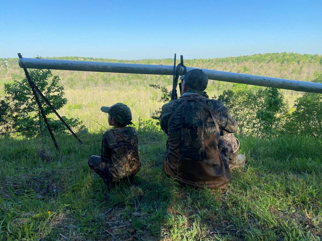 A father and son hunting turkeys in the woods.