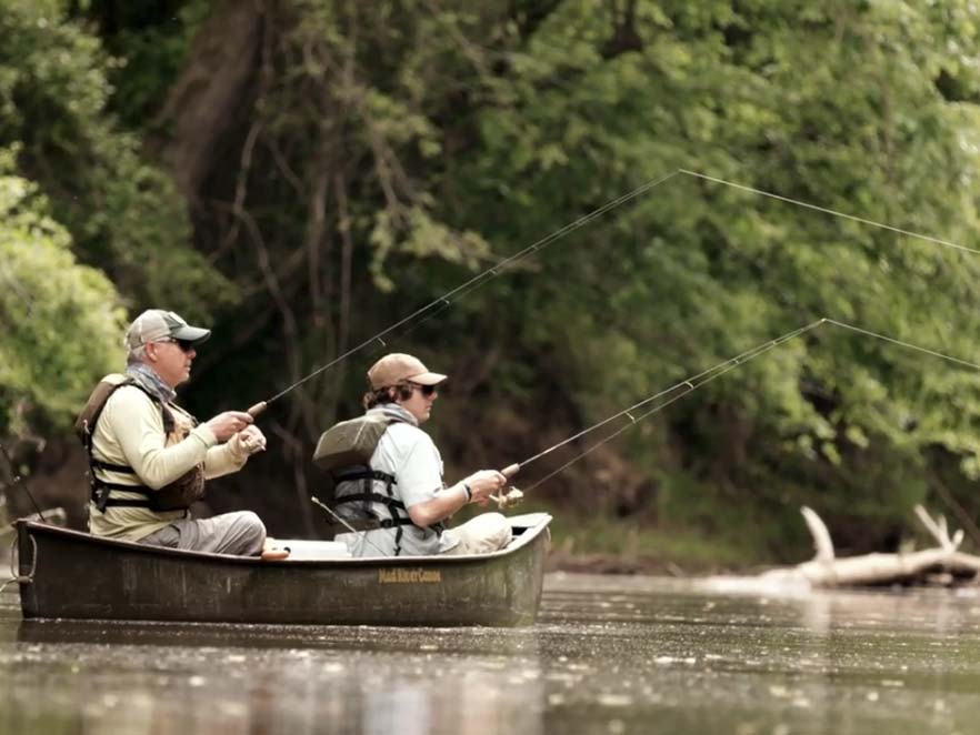 Two men fishing in a small boat on a creek.