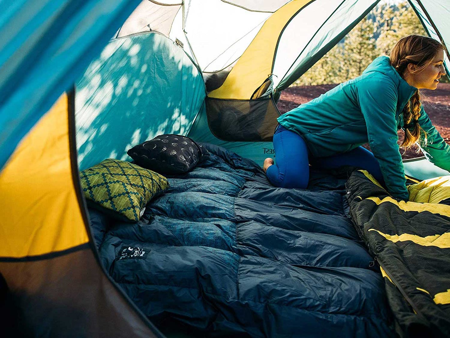 Woman in tent with sleeping bag and camping pillows.