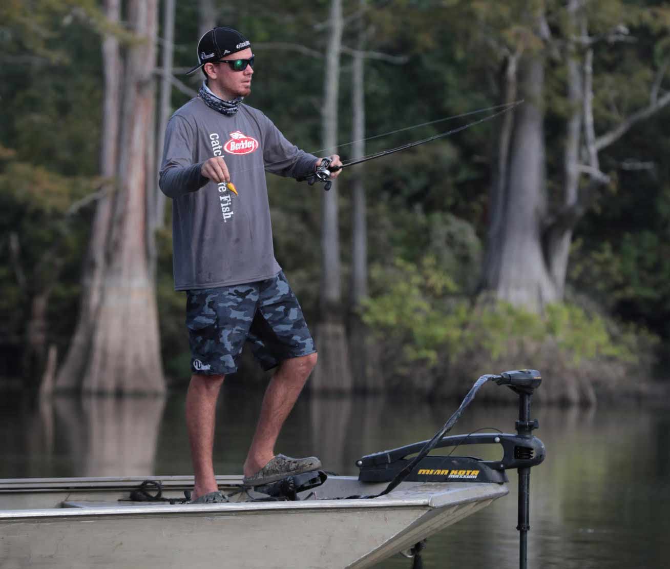 A bass angler stands at the front of a fishing boat getting ready to cast a line.