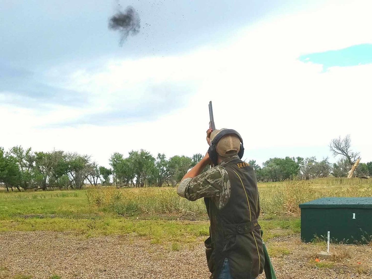 Man in a camo shooting skeet in a field.