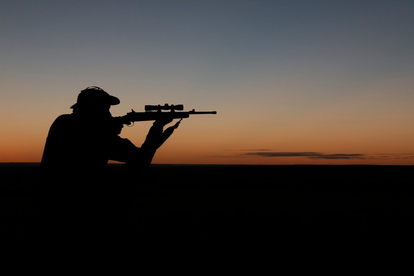 Silhouette of a man aiming a rifle against the sunset.