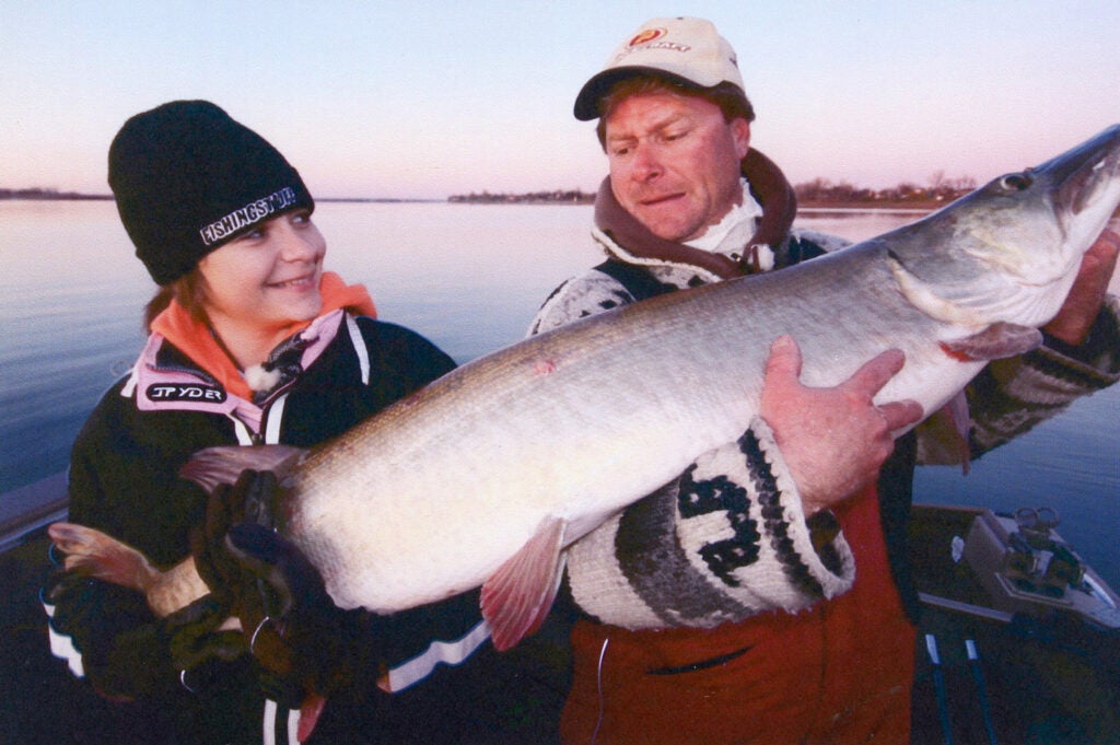 A man and young child holding up a large muskie fish.