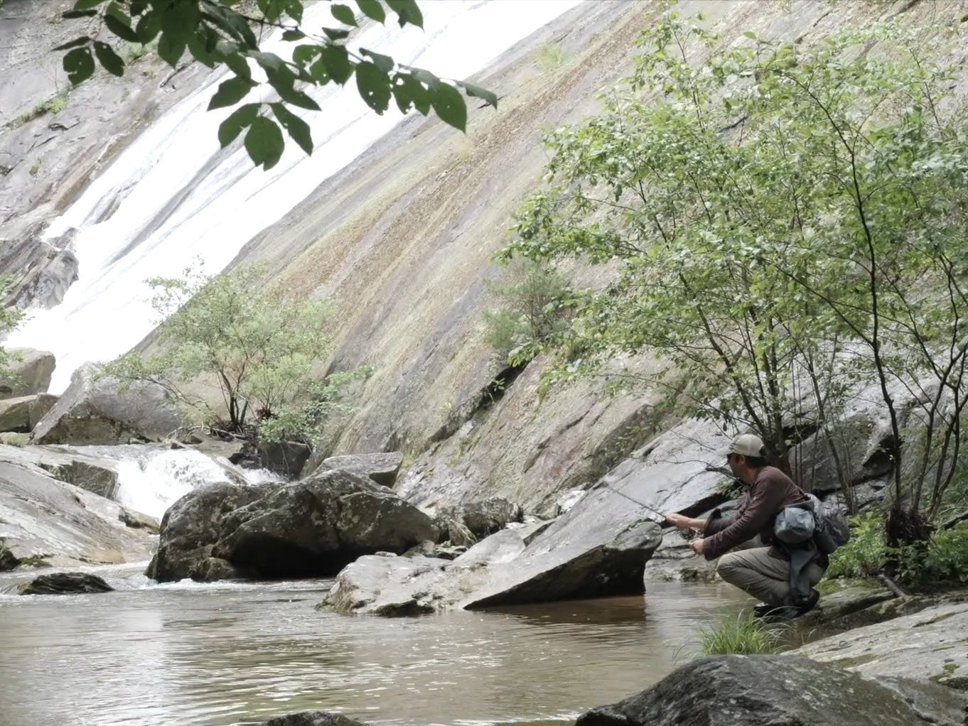 An angler fishing for trout near a waterfall and river.
