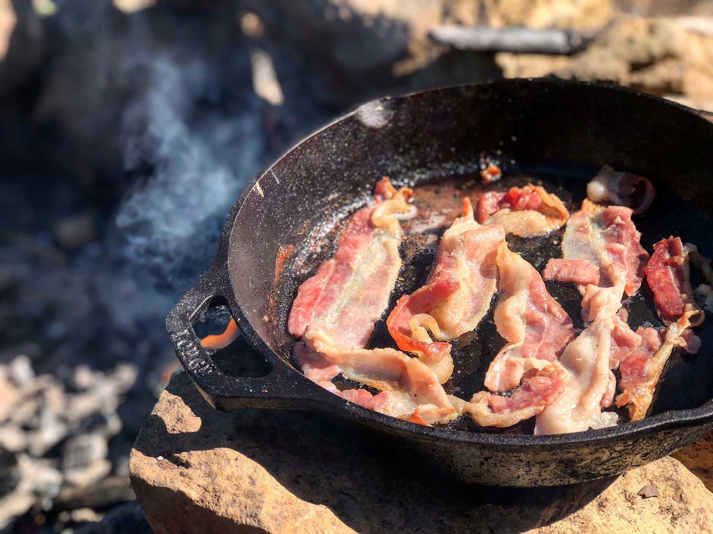 bacon cooking in a skillet on an open fire