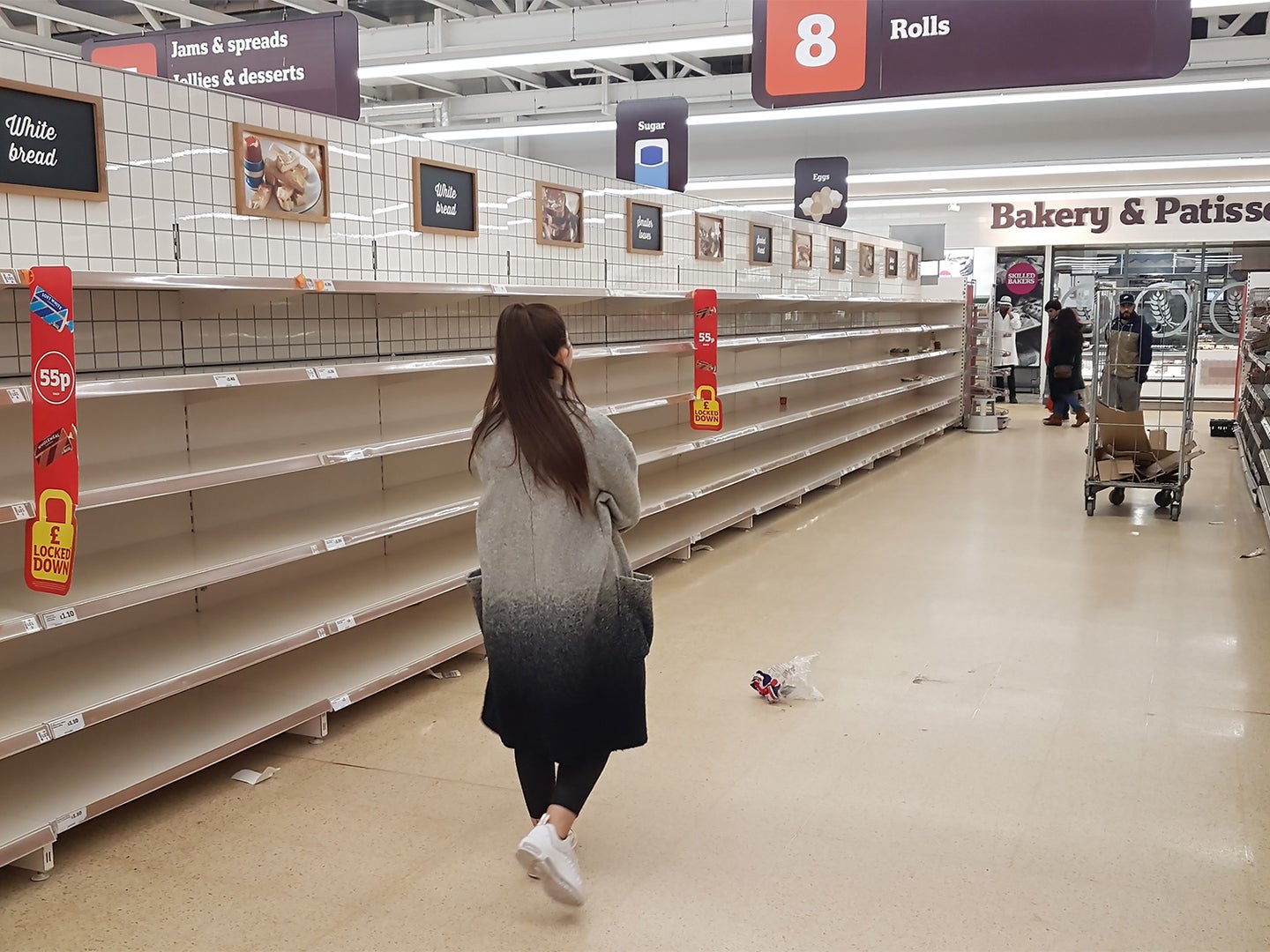 A woman walks through a grocery store aisle with empty shelves.