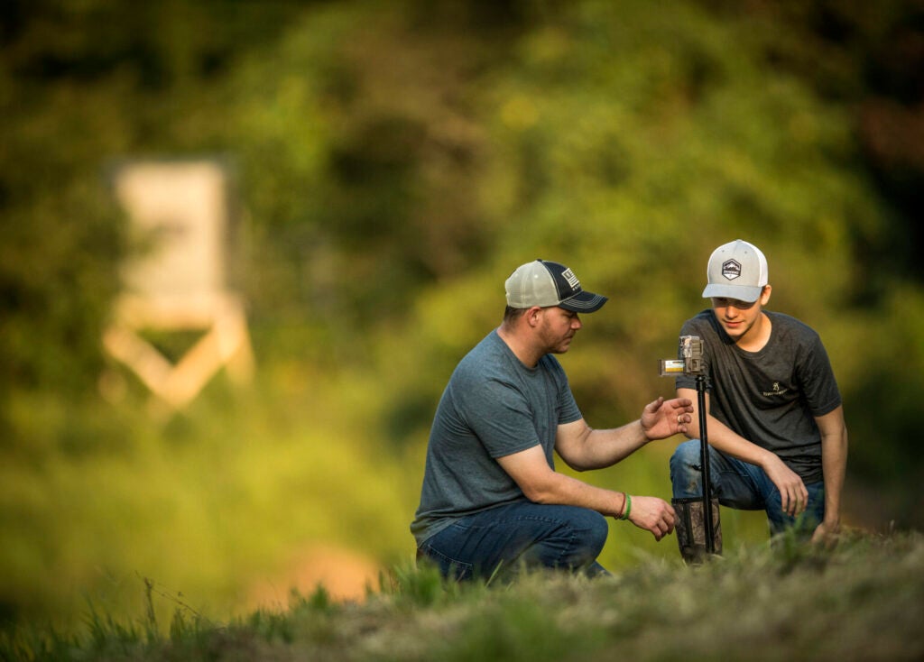 Man and boy setting up trail camera in a field.