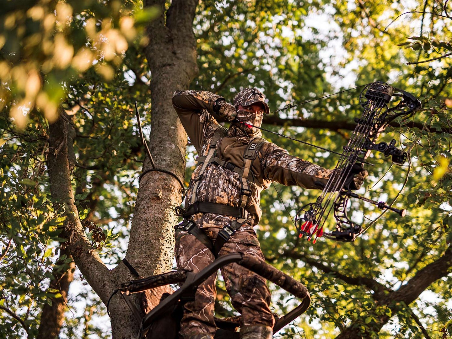 A hunter drawing on a crossbow on a hunt stand in a tree.