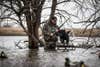 A hunter stands beside a hunting dog as it leaps into the water.