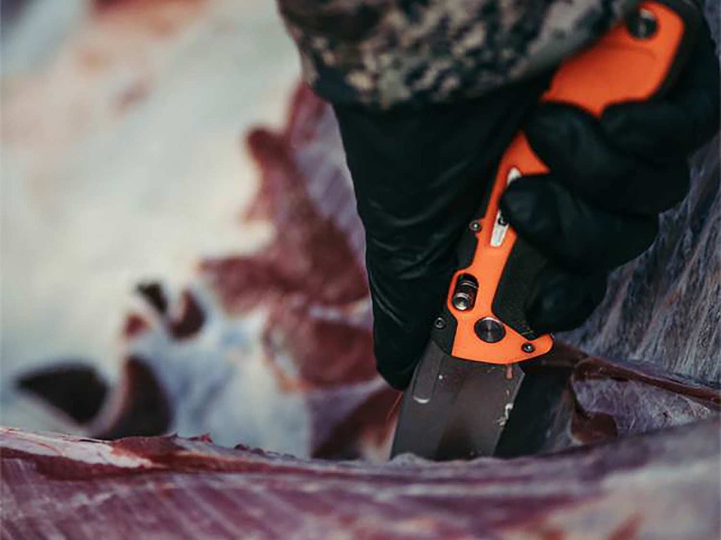 A hand pulling a knife through wild game meat to separate the skin from the meat.
