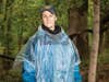 A female hunter in a blue jacket and plastic waterproof poncho stands in the woods outside.