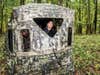 A woman and man hunter bunker down in a hunting blind in the woods.