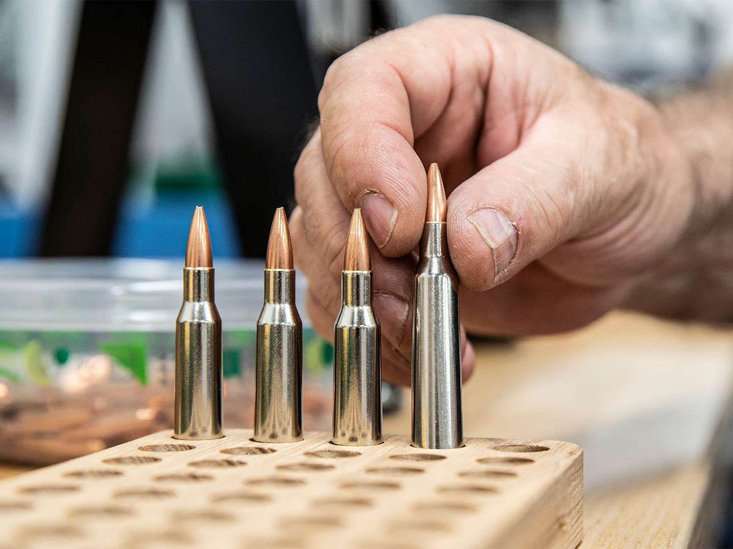 A hand places custom bullets into a wooden plank with holes drilled into it.