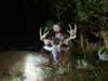 A hunter kneels behind a dead whitetail deer and holds up its head by the antlers.