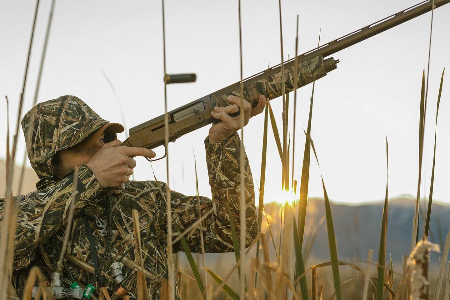 A hunter with a shotgun aims it into the air.