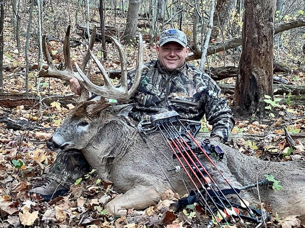 A hunter kneels behind a large buck.