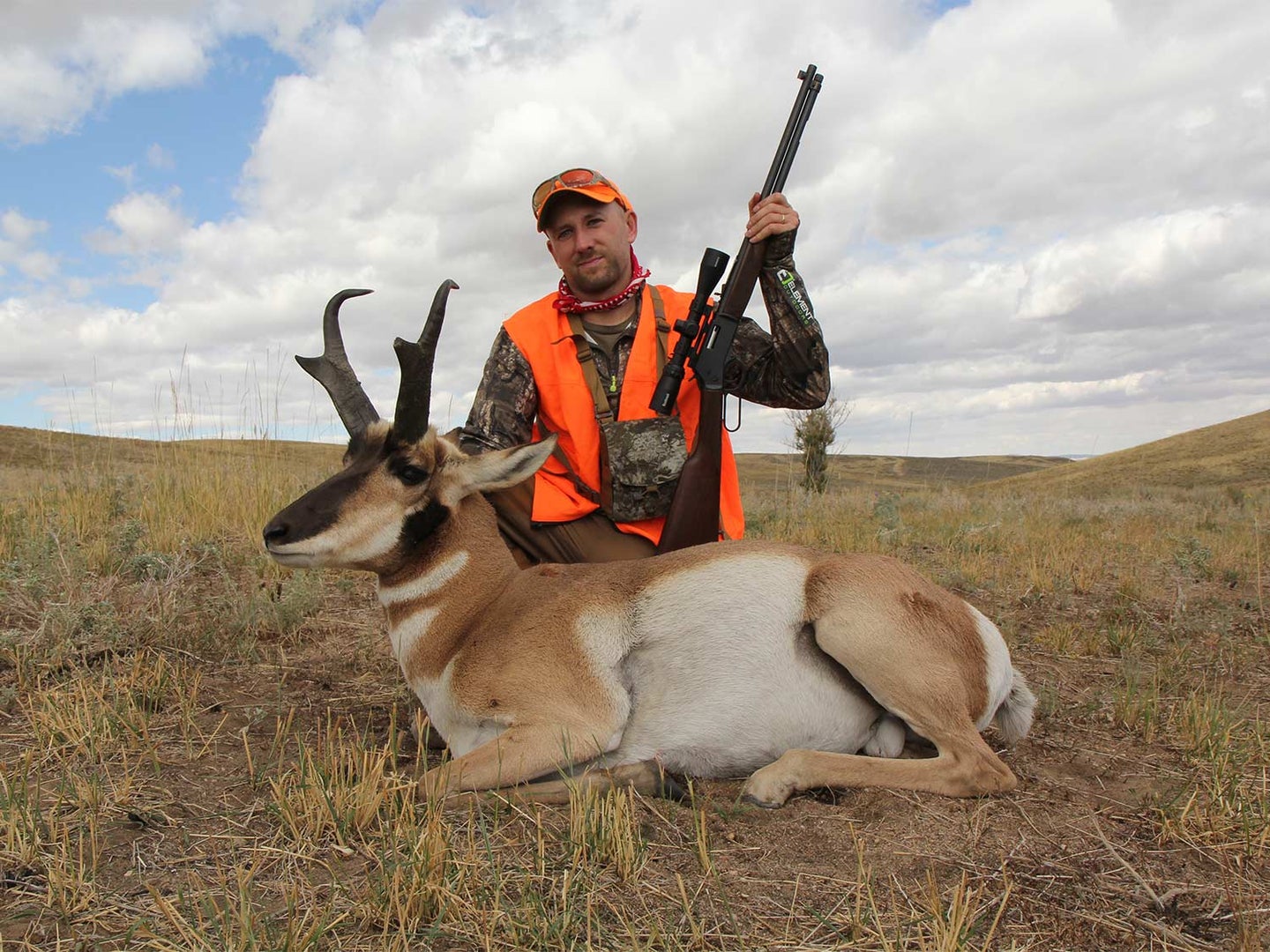 A hunter kneels behind a large antelope in an open field.