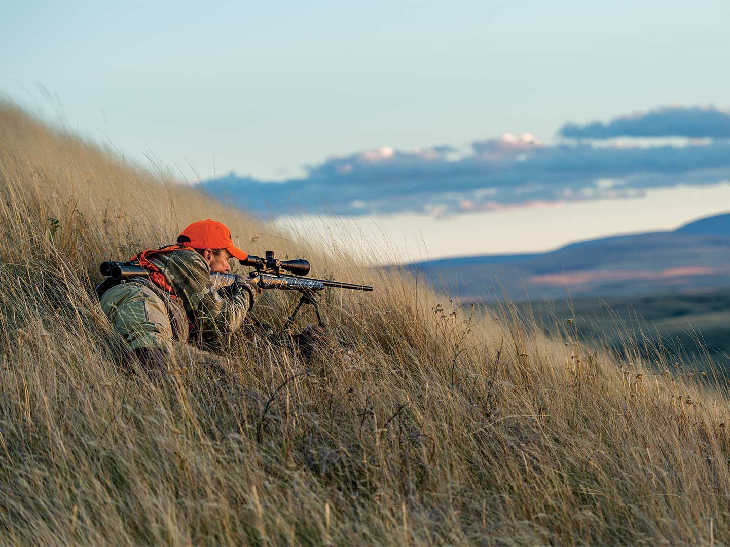 A hunter aims a rifle on the hillside.