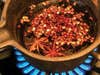 A small pot of chili, oil and star anise on a small cooking burner.