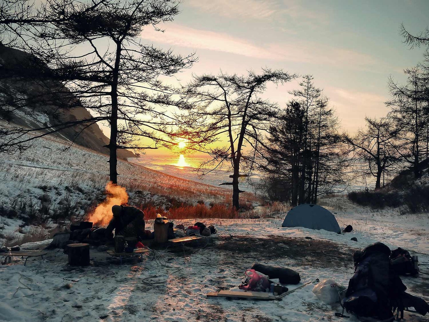 A wintry landscape with a small campsite and burning fire.