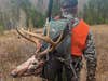 A hunter walks through a field with a deer head strapped to his back.