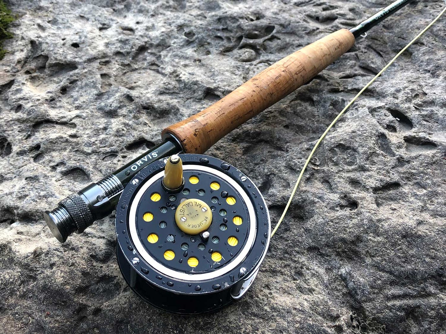 An Orvis reel and Pflueger fly reel on a stone by the water.