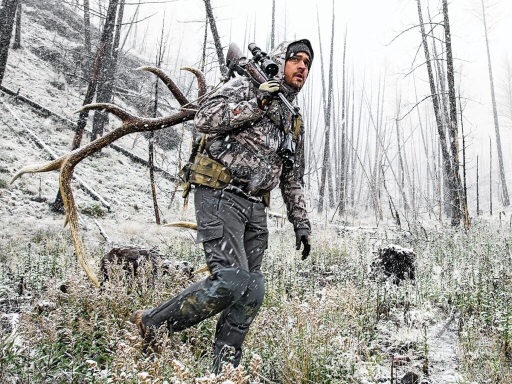 A hunter walking through snowy woods.