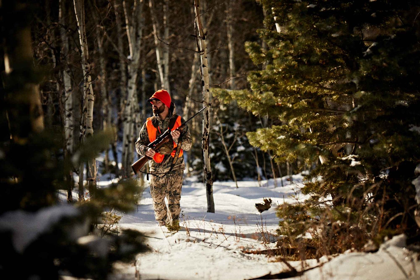 Hunter wearing orange vest, walking in the snow