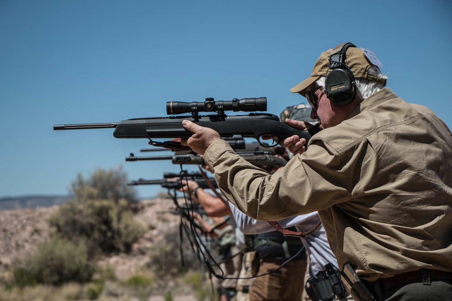 A line of men aim scout rifles at a shooting range.