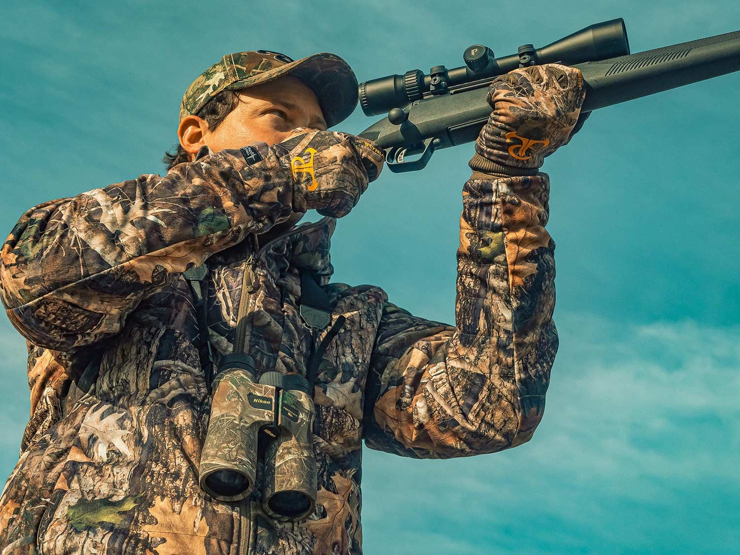 A hunter holds a rifle up to their shoulder.