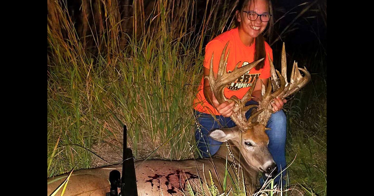 A young girl poses next to a whitetail buck.