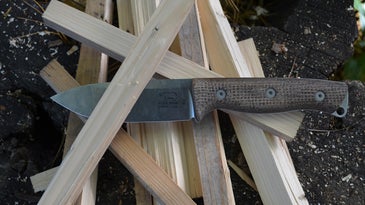 A bushcraft knife in a pile of wood pieces.