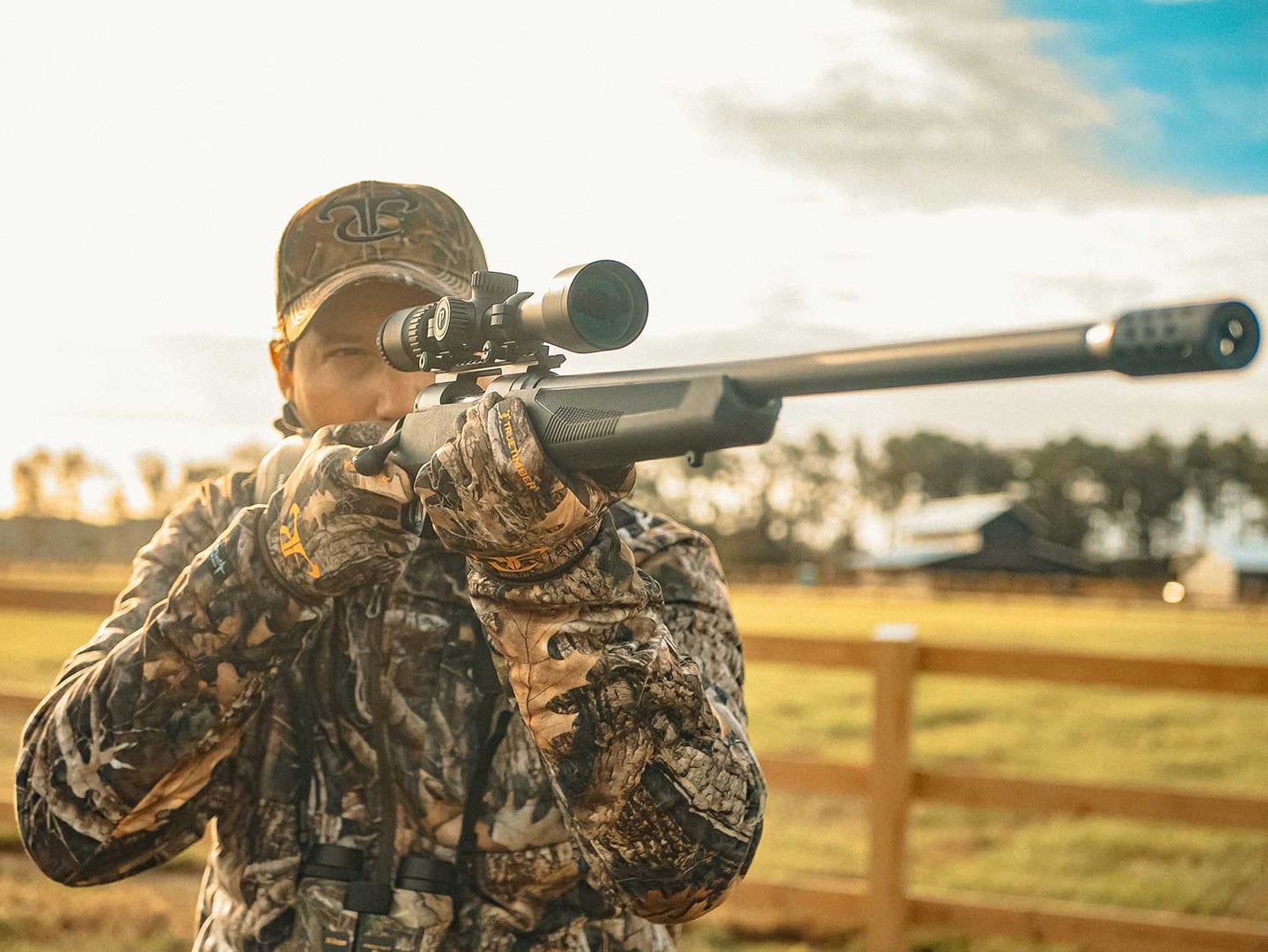 A deer hunter in full  camo aims a rifle in a field.