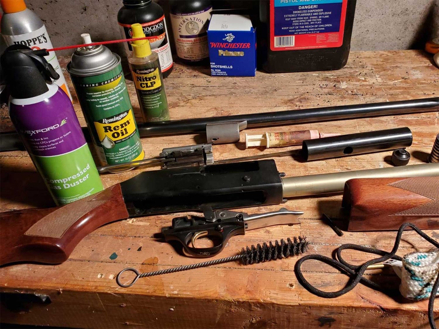 A disaassembled shotgun on a table next to cleaning supplies and tools.