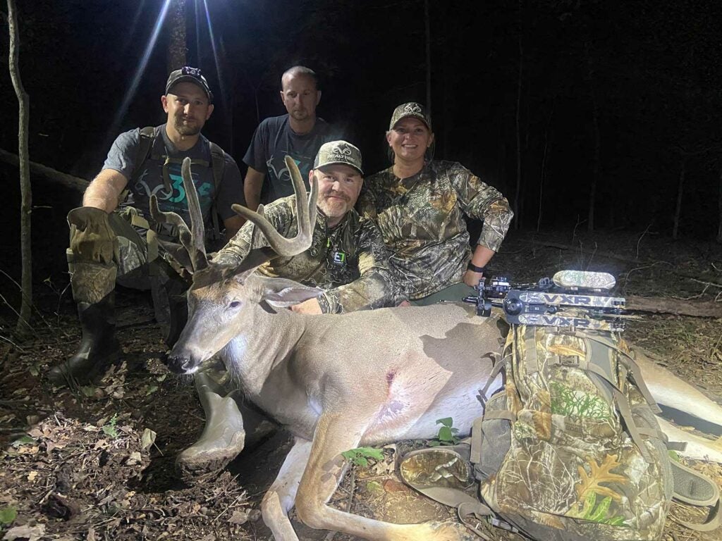 A group of hunters kneel behind a large whitetail buck with velvet antlers.